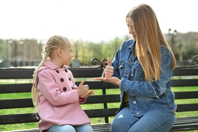 Mãe e filha surda conversando em Libras num banco de praça