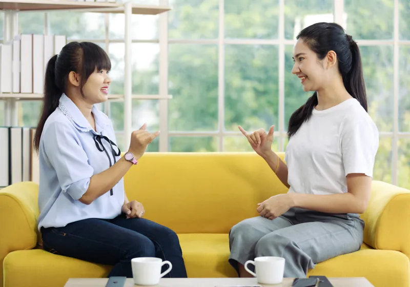 Duas mulheres conversando em Libras sentadas num sofá